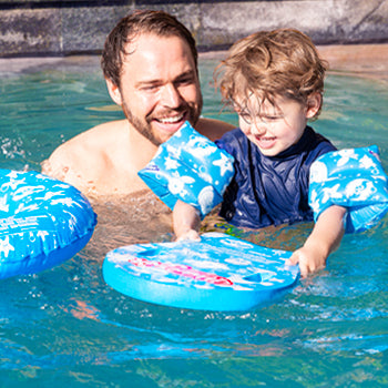 Father teaching child to swim in pool with wahu jnr kickboard and inflatable armbands